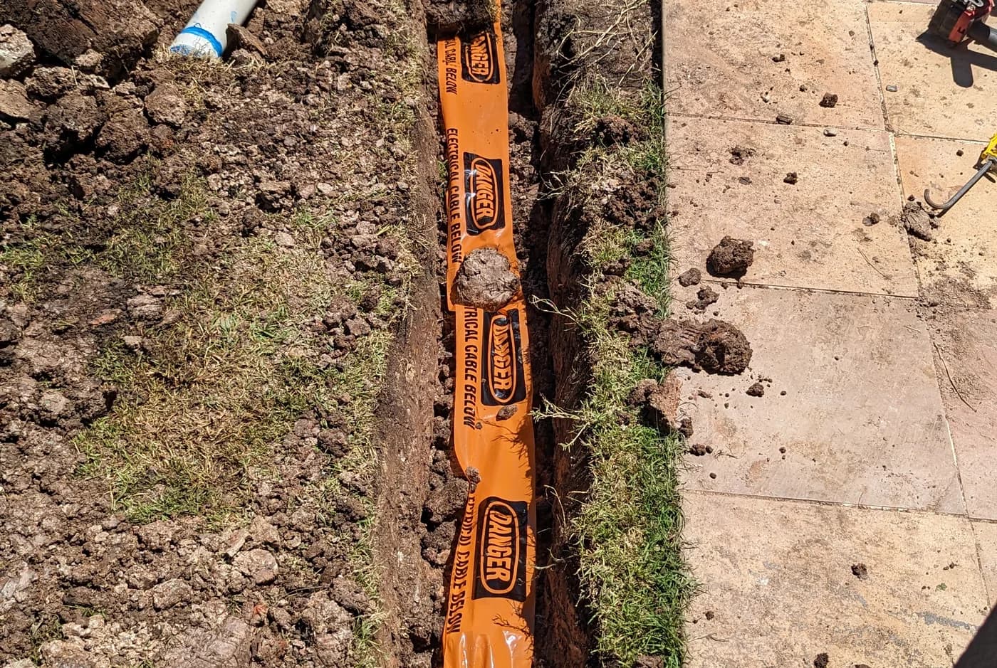 Orange conduit laid in a trench running across a yard