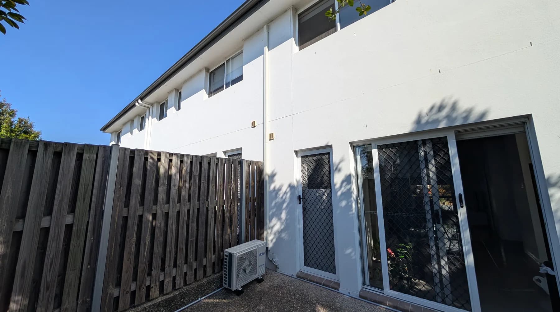 A row of rendered townhouses with a split-system condenser along the side path