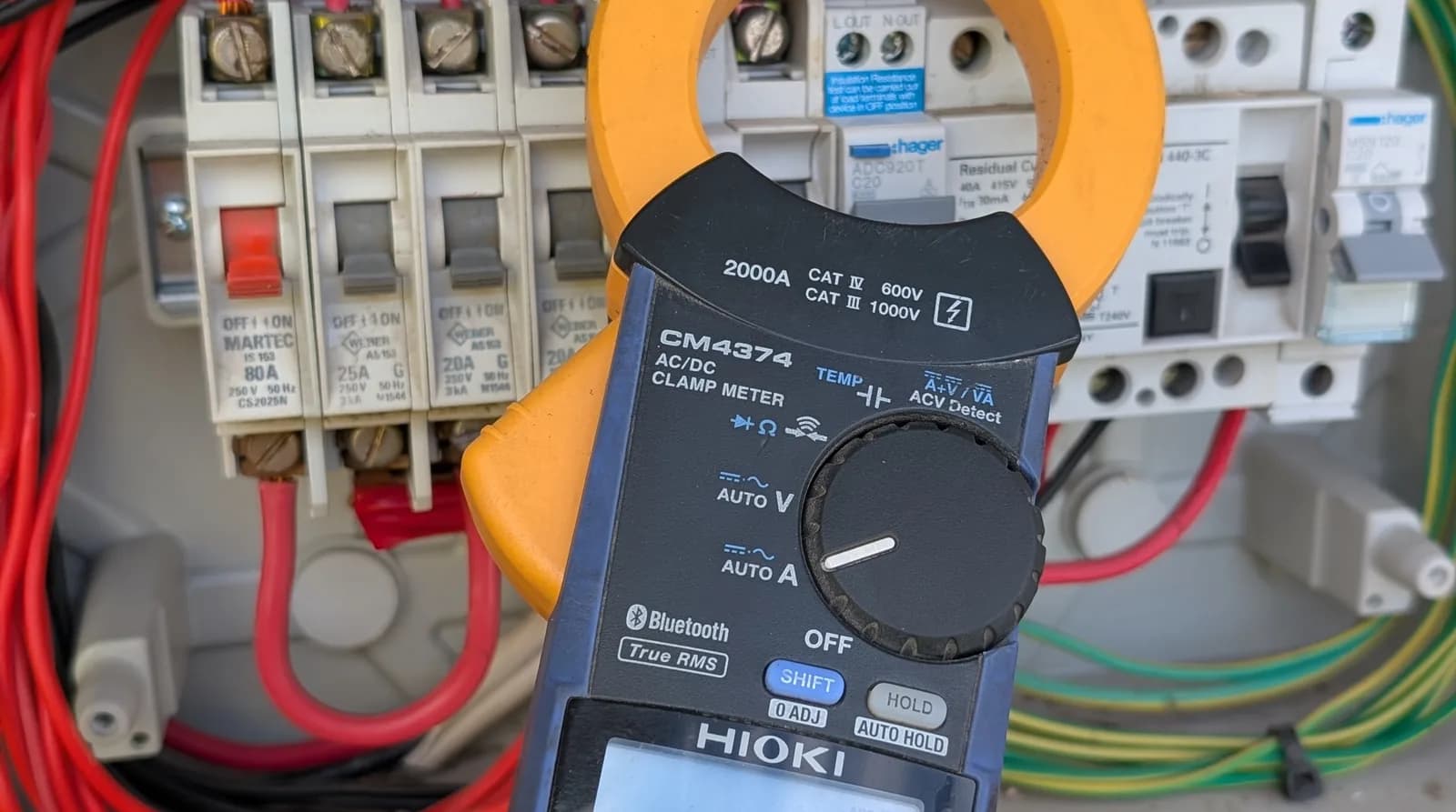 A clamp meter taking a current reading inside an open switchboard