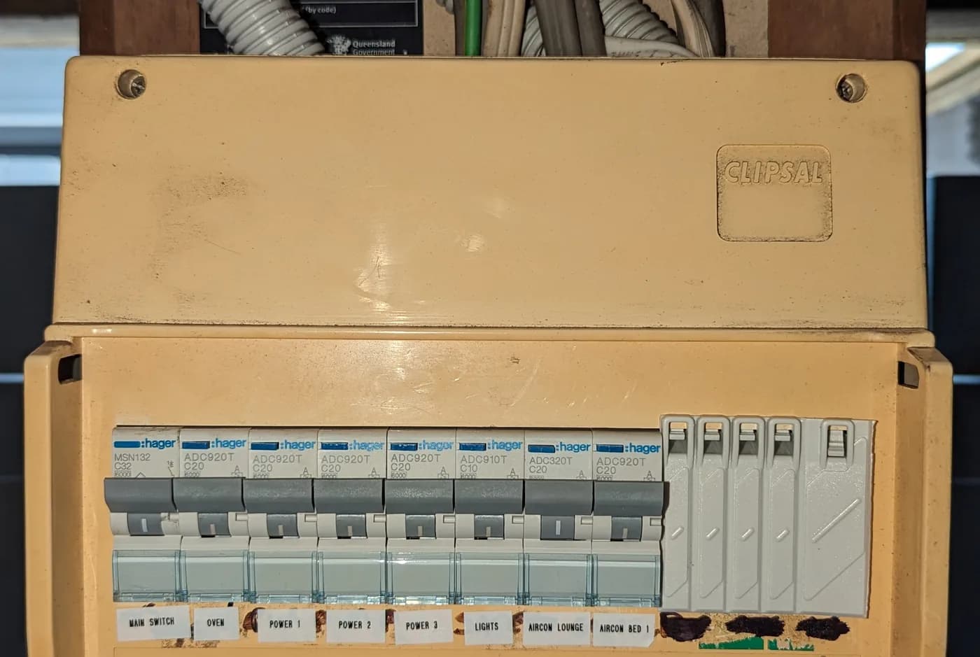 An older switchboard enclosure with modern breakers fitted and the supply conduits above