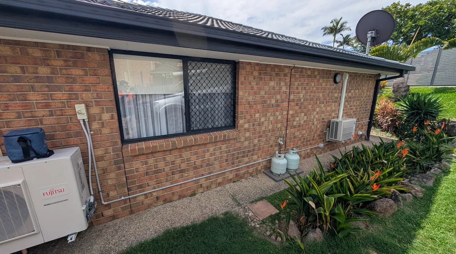A single-storey brick Brisbane home with a split-system condenser beside the wall