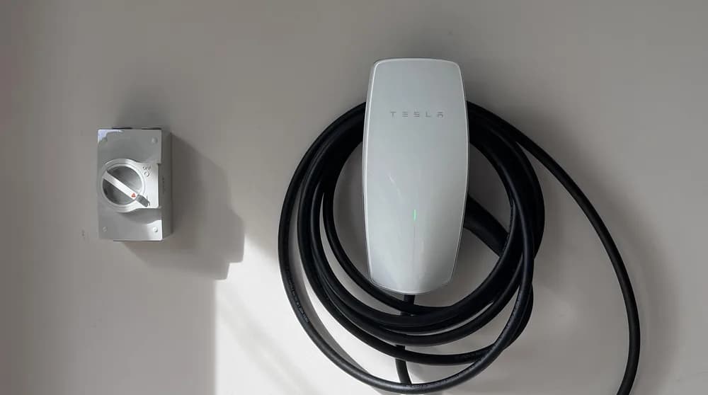 A slim white EV wall connector mounted on an interior wall
