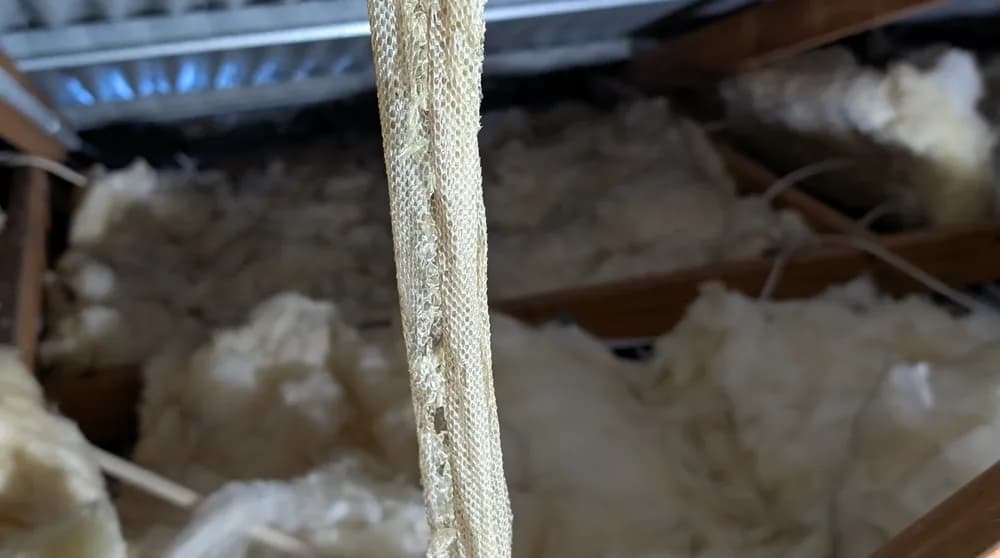 Perished rubber-insulated cable running through roof-space insulation