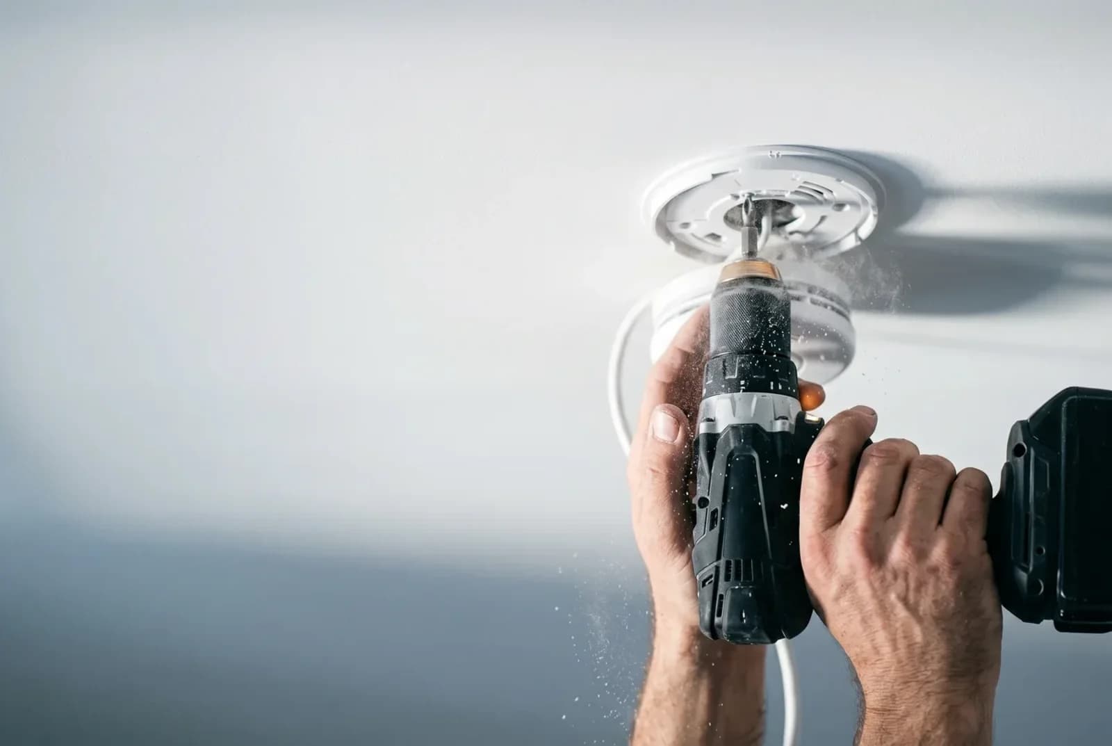 A photoelectric smoke alarm being fixed to a ceiling with a cordless drill