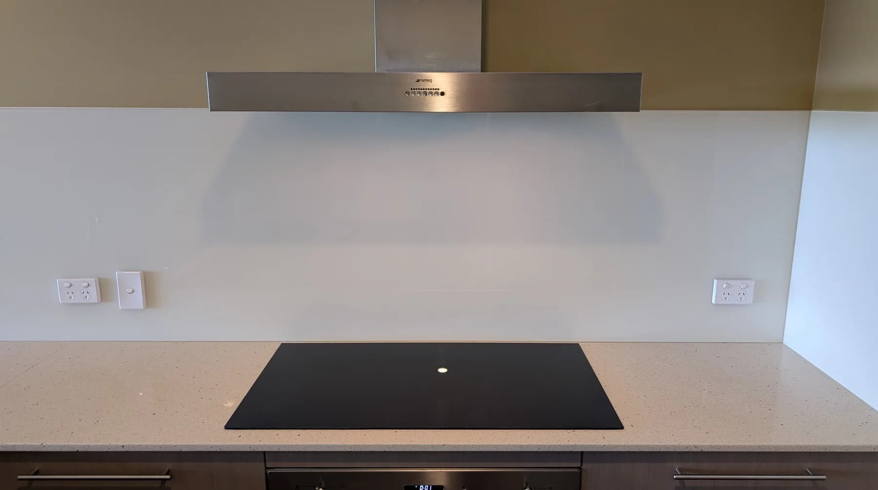 A ceramic cooktop and stainless rangehood in a finished kitchen