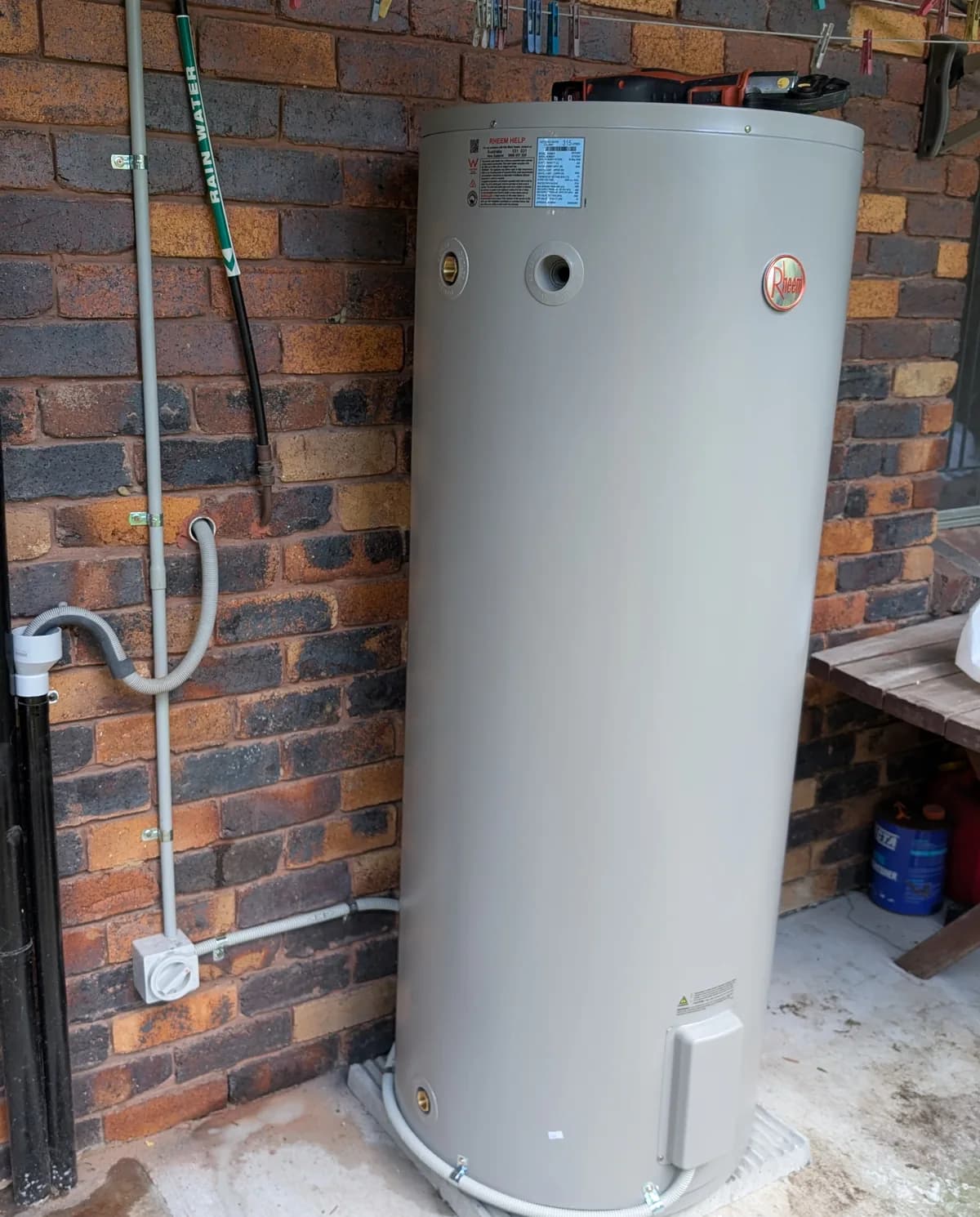An electric hot water cylinder installed against a brick wall