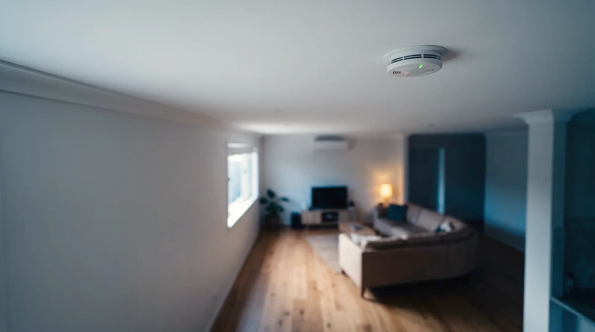 A flush-mounted photoelectric smoke alarm on the ceiling of a Brisbane living room at dusk