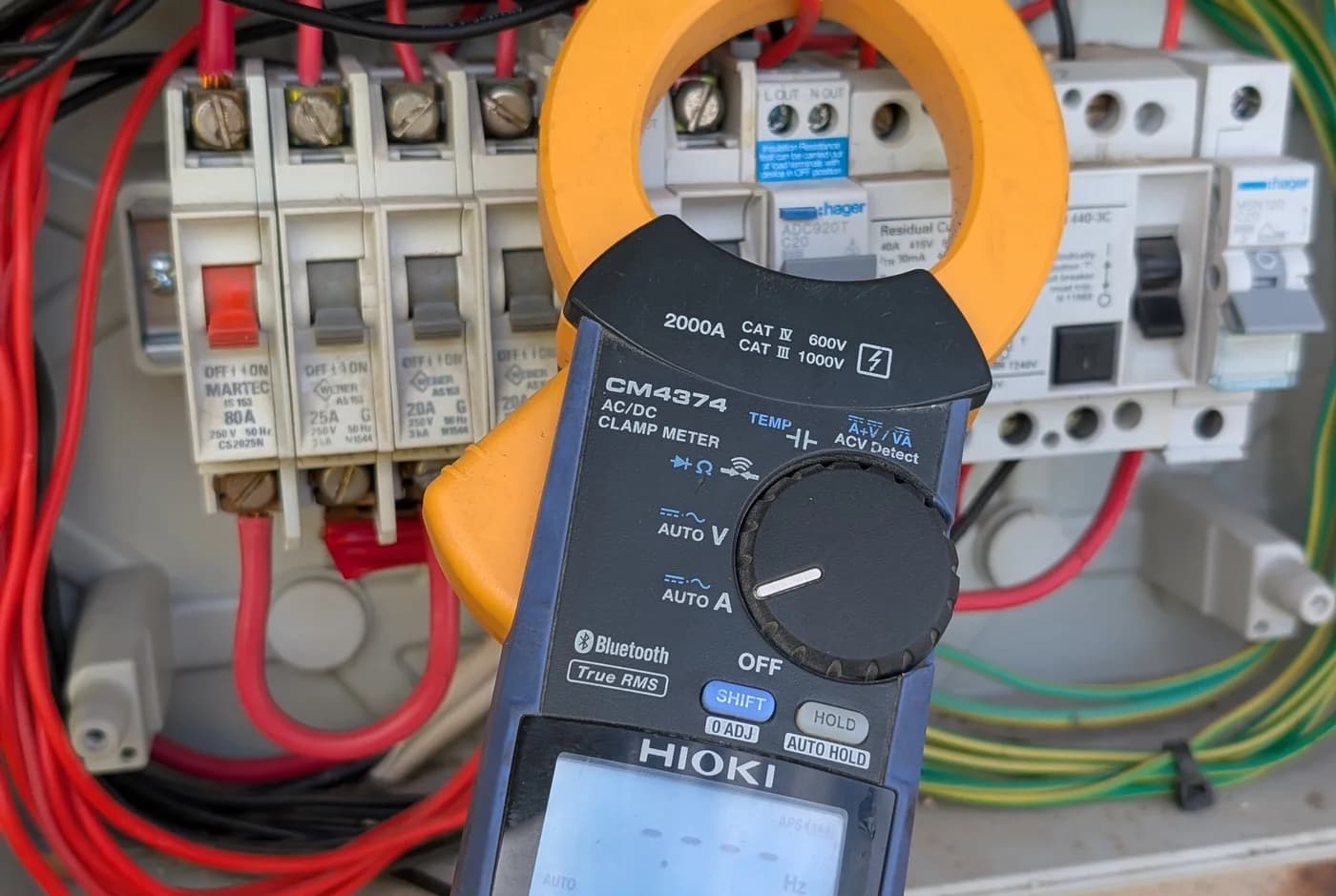 A clamp meter taking a live reading across the breakers in a switchboard