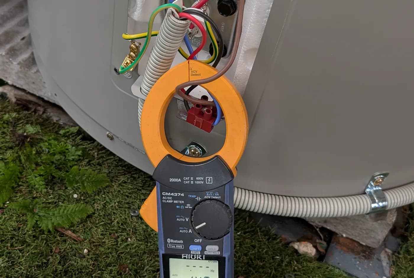 A clamp meter testing at the element access plate of a hot water cylinder